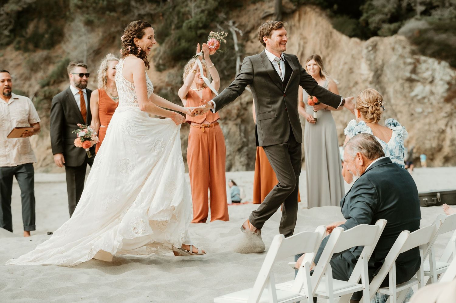 Wedding ceremony setup with white chairs on rocky beach landscape.