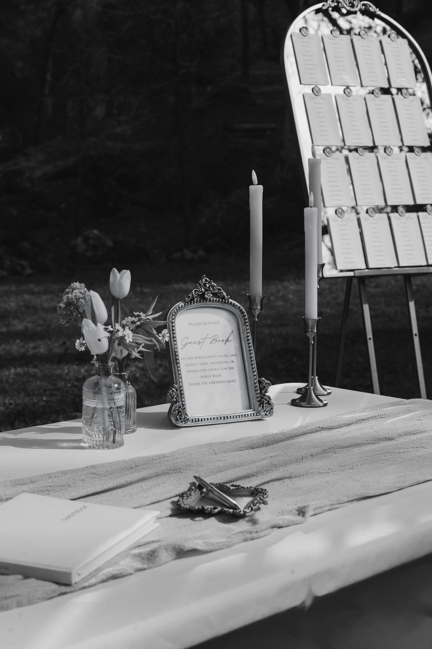 A black and white photo of a wedding seating chart display with candle and vintage frame.