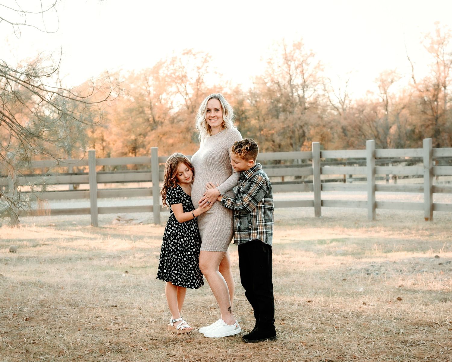Romantic couples embrace during a warm sunset photo session in a rustic field with wooden fences.