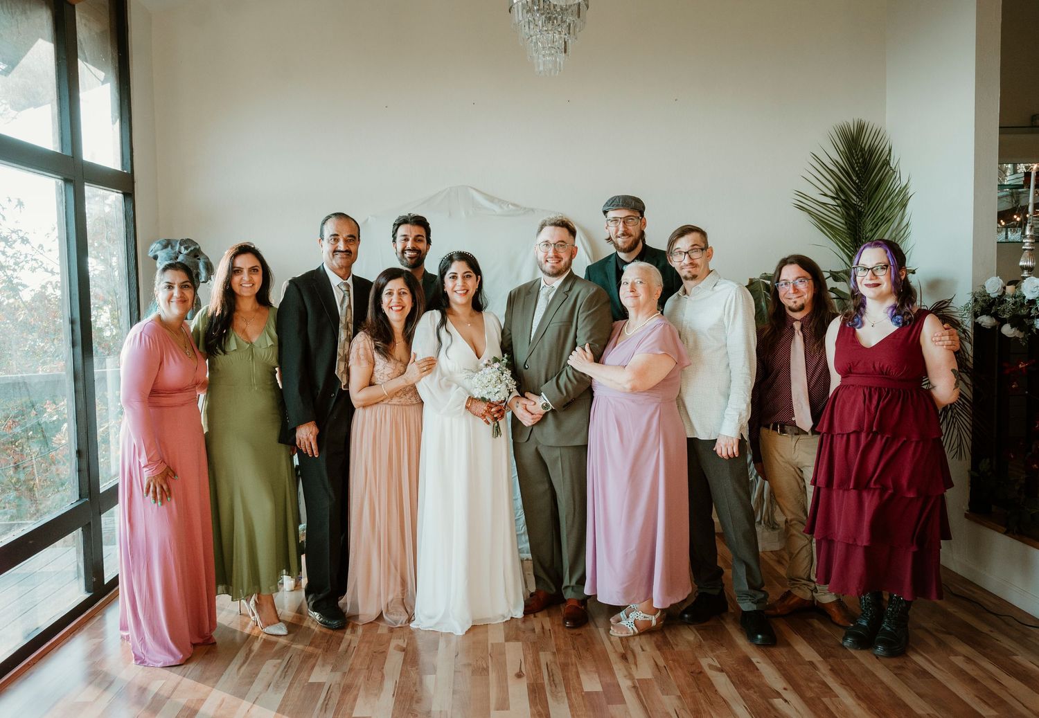 Wedding party in coordinated pink and burgundy dresses posing together in a bright indoor space.