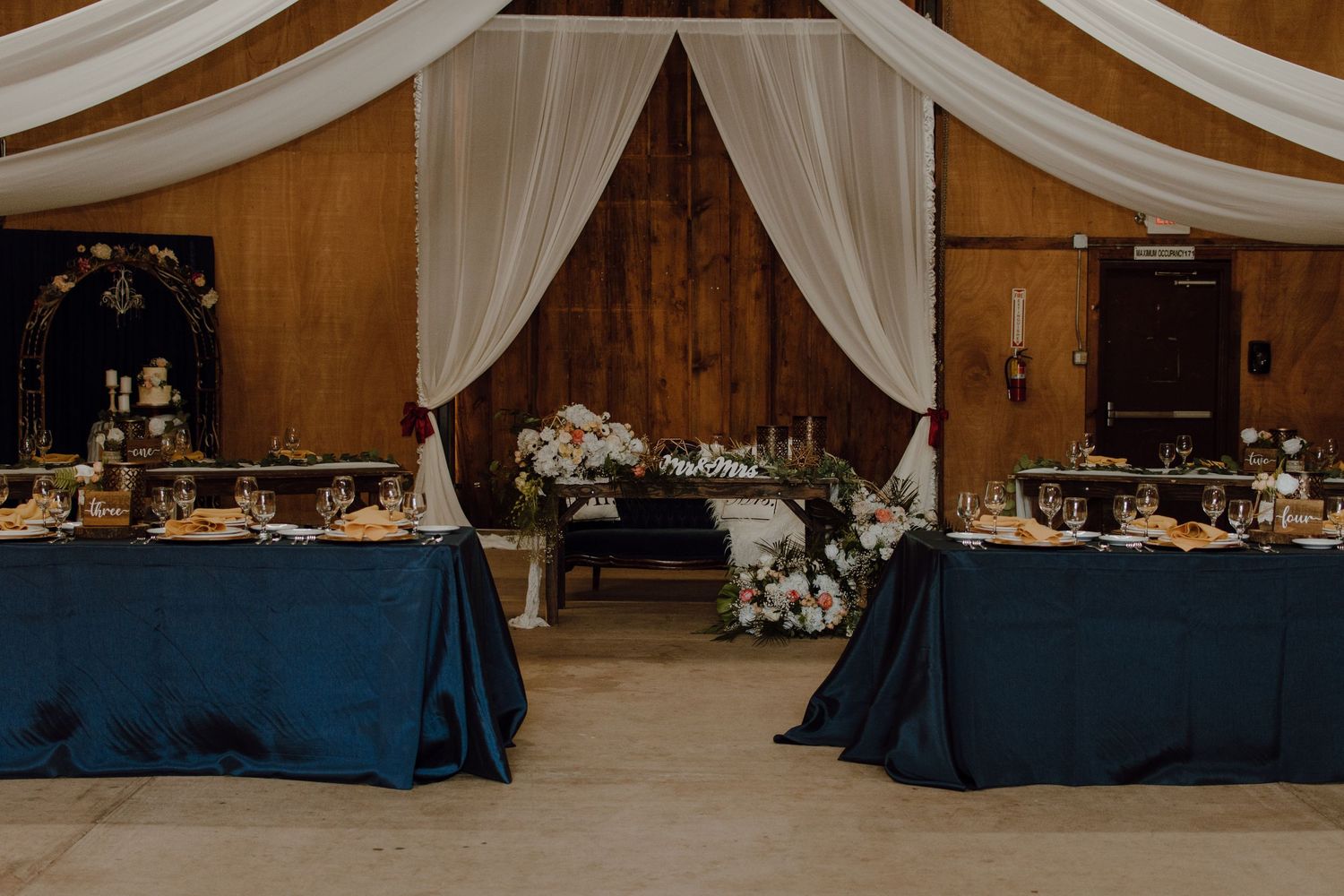 Wedding reception hall with navy blue tablecloths and white draped fabric decorations.