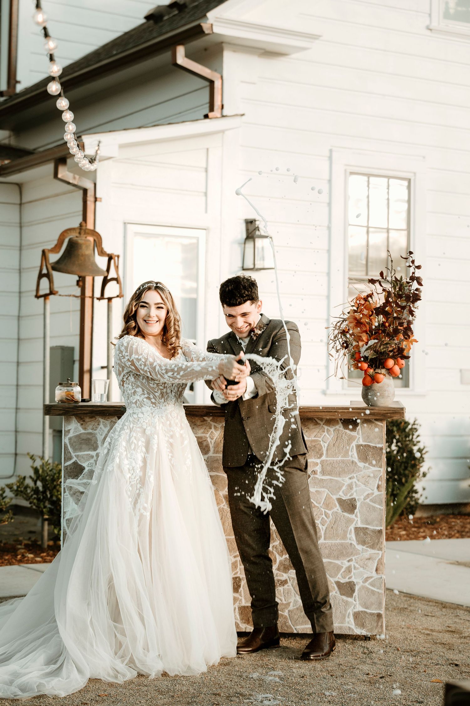 A couple celebrating with champagne outside a charming white farmhouse.