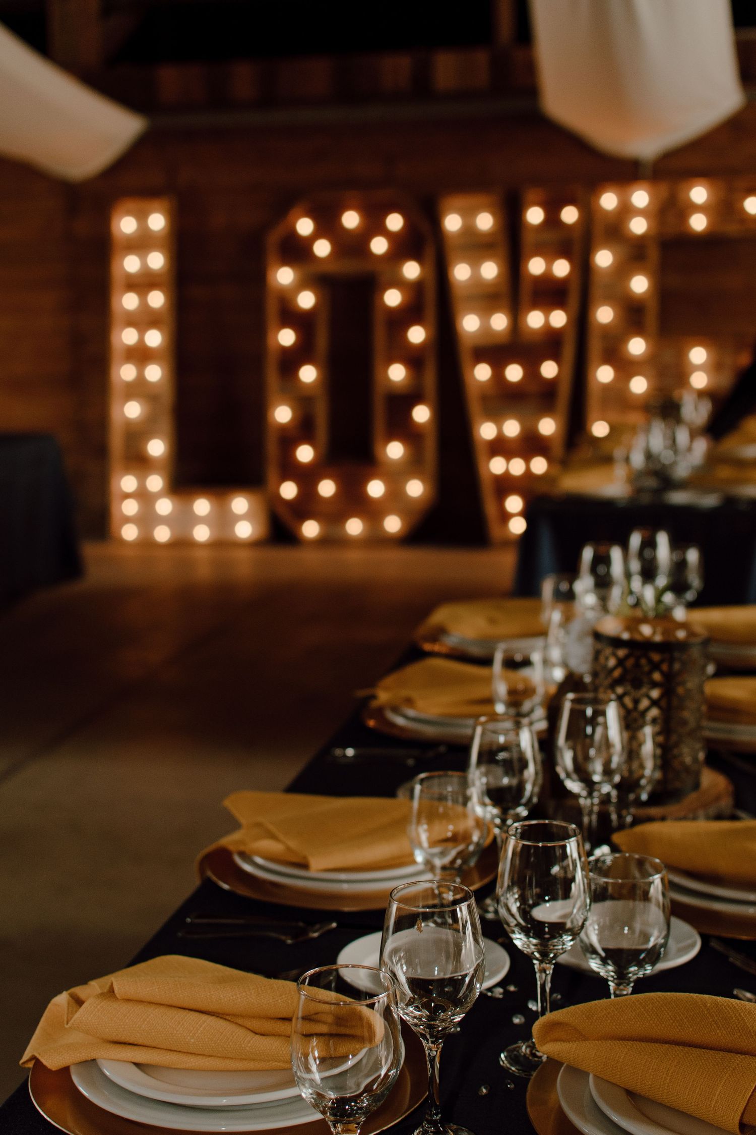 Illuminated LOVE marquee letters behind an elegant table setting with yellow napkins.