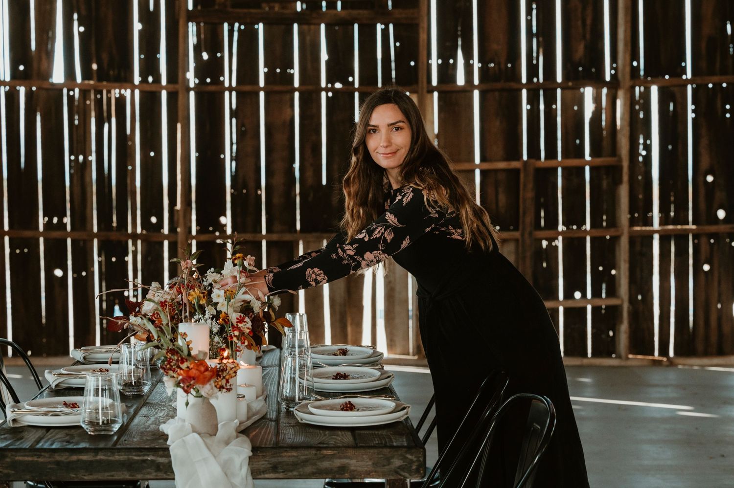 Event styling scene with floral arrangement and place settings in rustic barn venue.