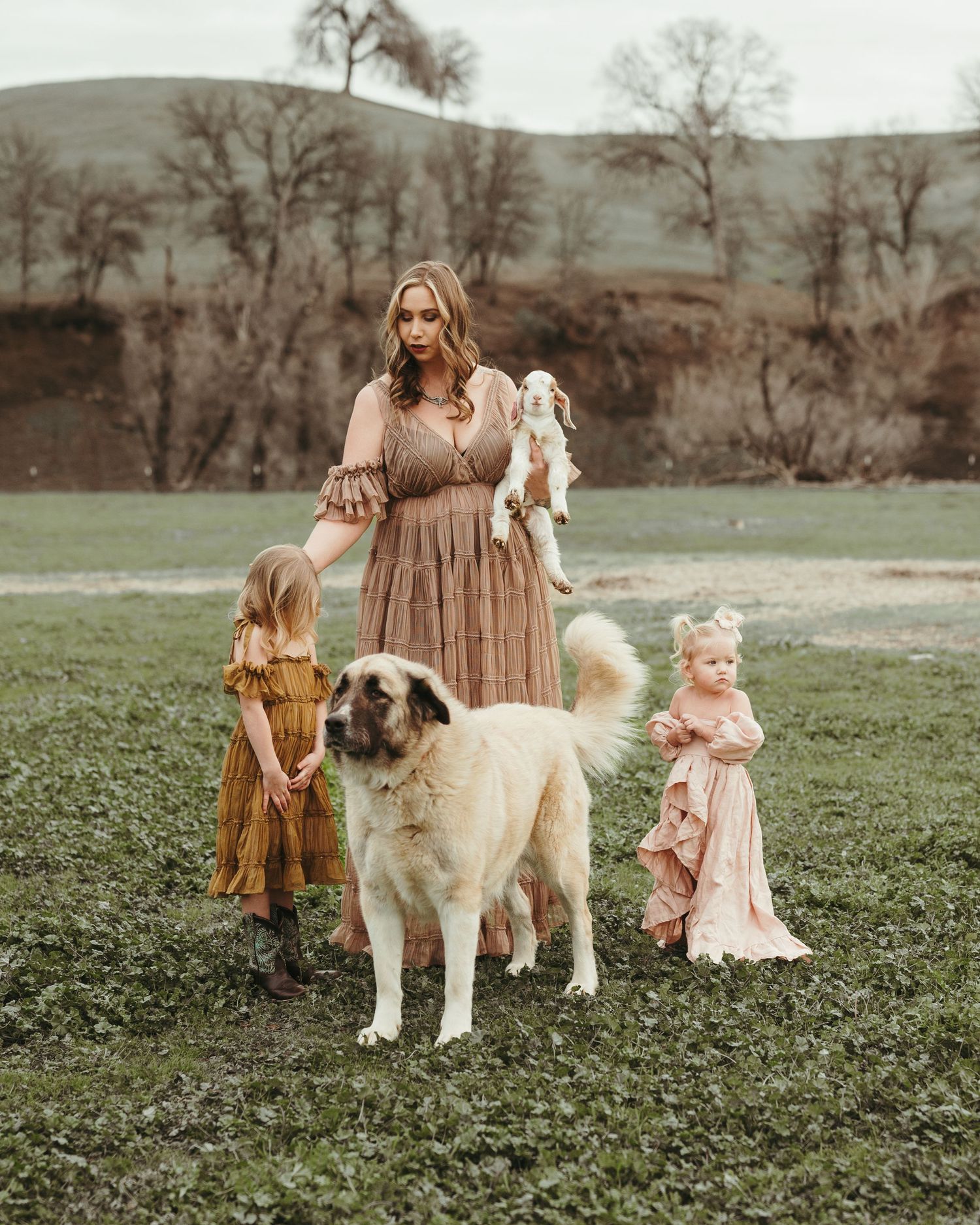 A family portrait in a field with children and a large dog against a scenic backdrop.