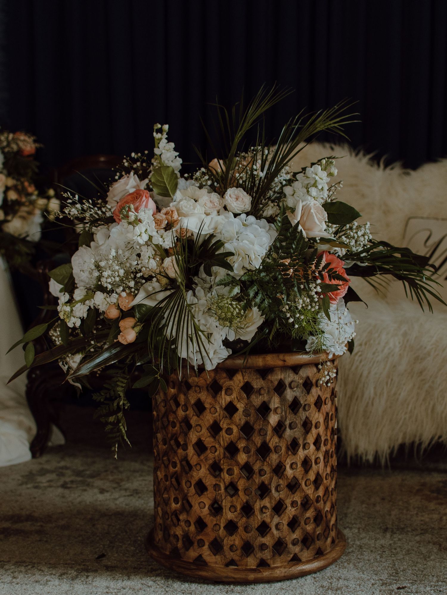 Elegant floral arrangement in a decorative woven bamboo vase featuring white hydrangeas and tropical greenery.