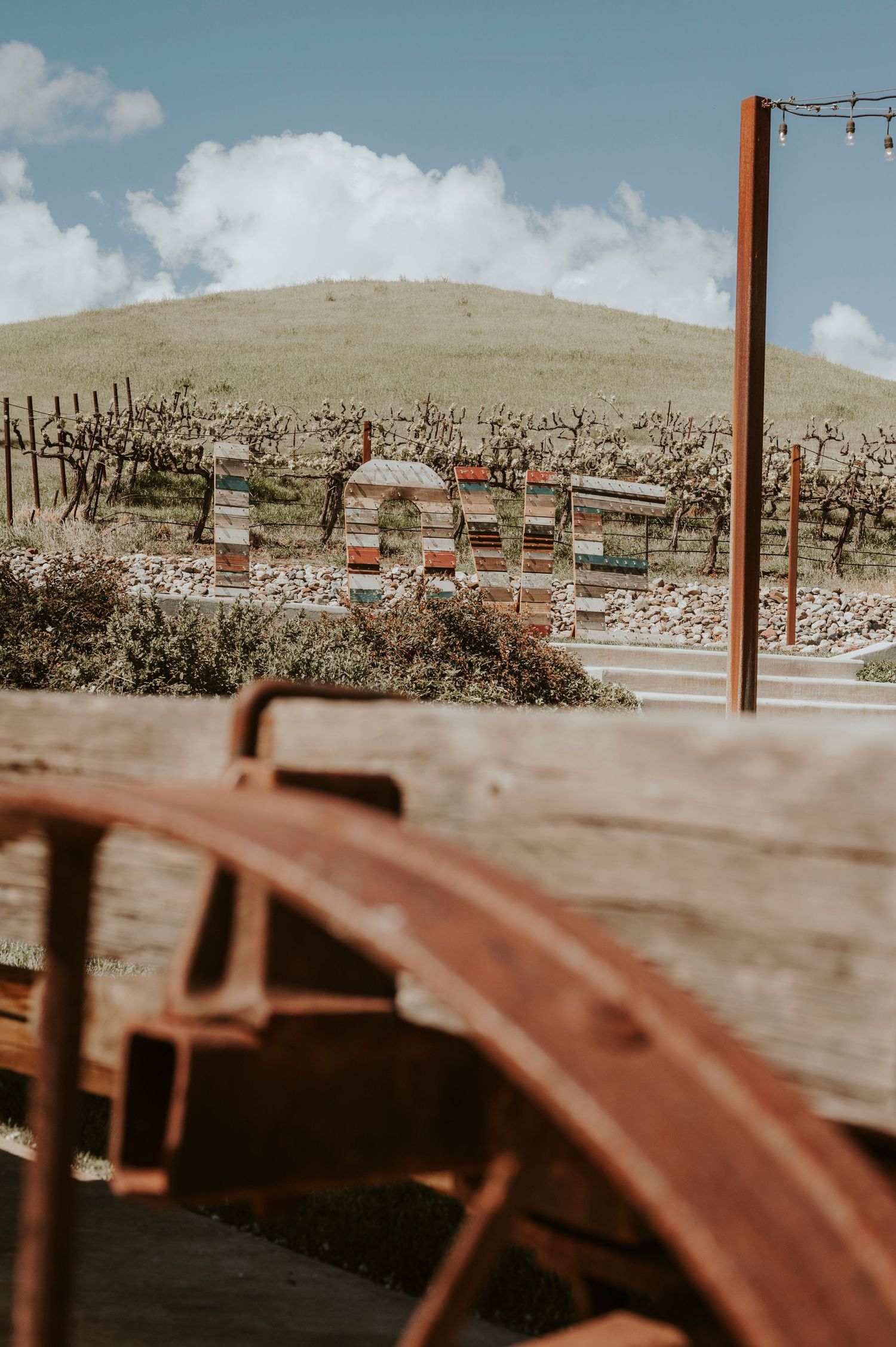 Wooden beehive boxes arranged in rows on a hillside under a blue sky with white clouds.