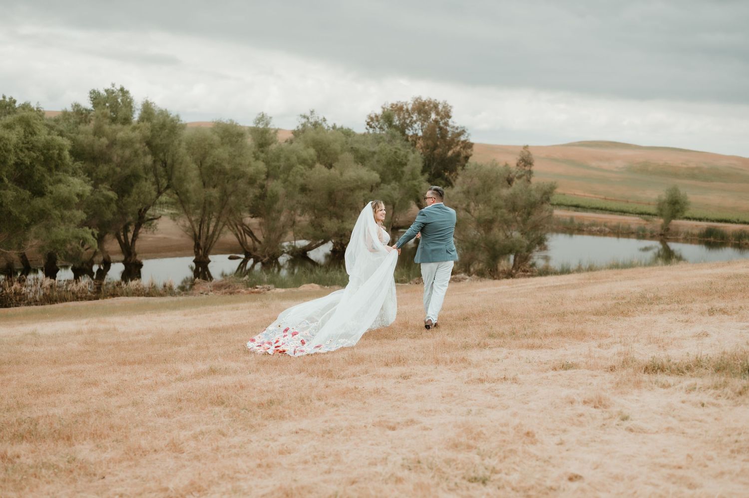 Wedding couple walking through rural landscape with dramatic cloudy sky.