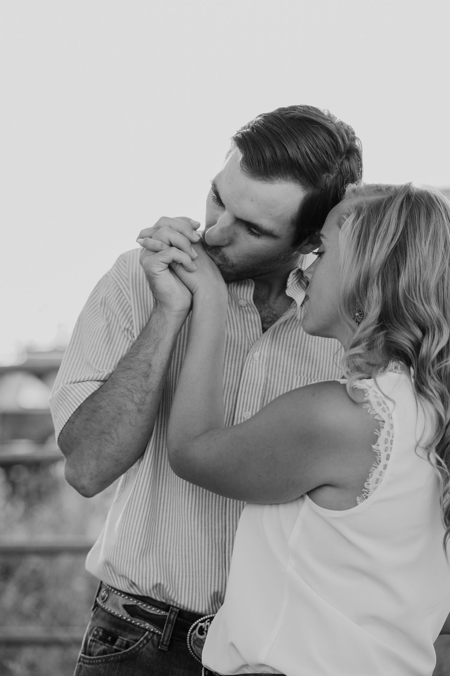 Black and white romantic photo of a couple dancing together outdoors, with one kissing the other's hand.