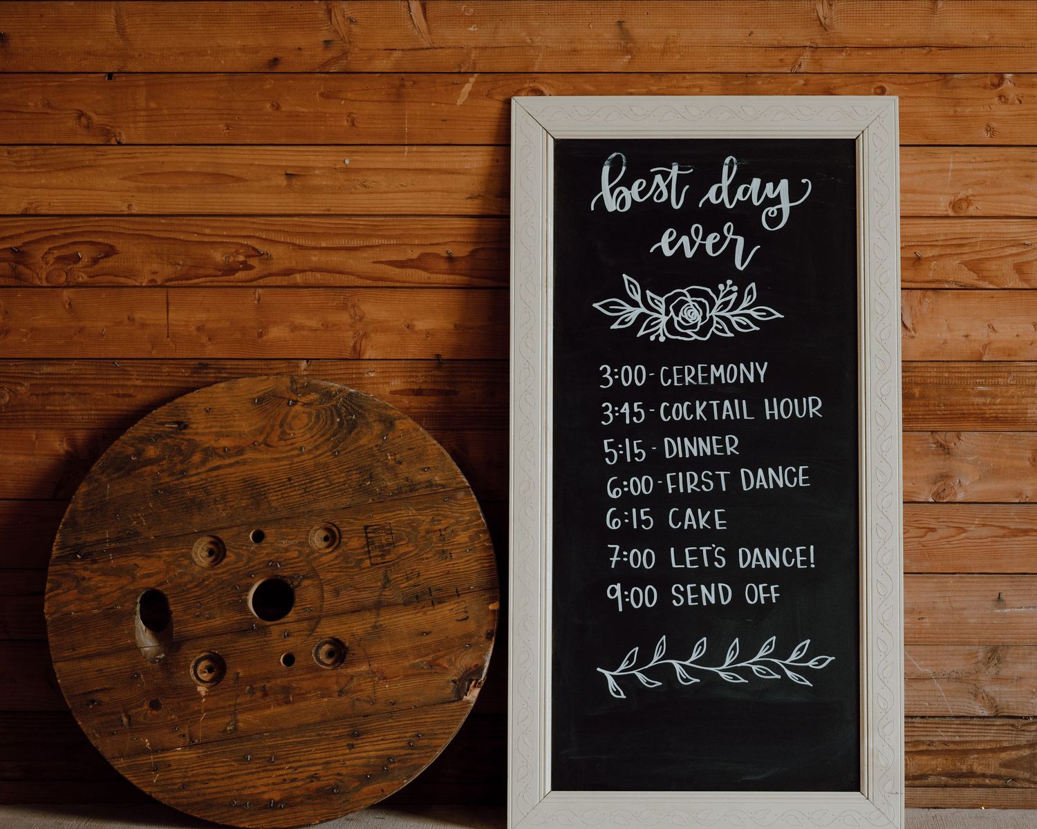 Wedding day timeline written on a chalkboard next to a rustic wooden spool.
