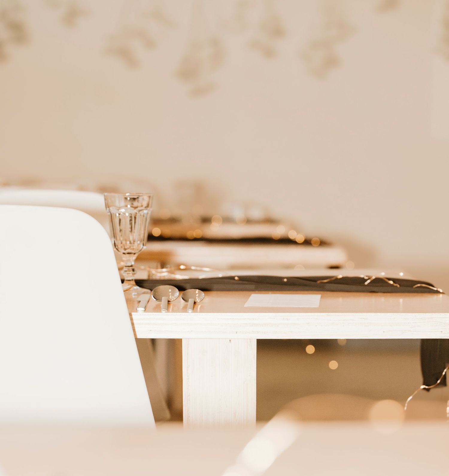 Minimalist table setting with crystal glassware and white chairs in soft lighting.