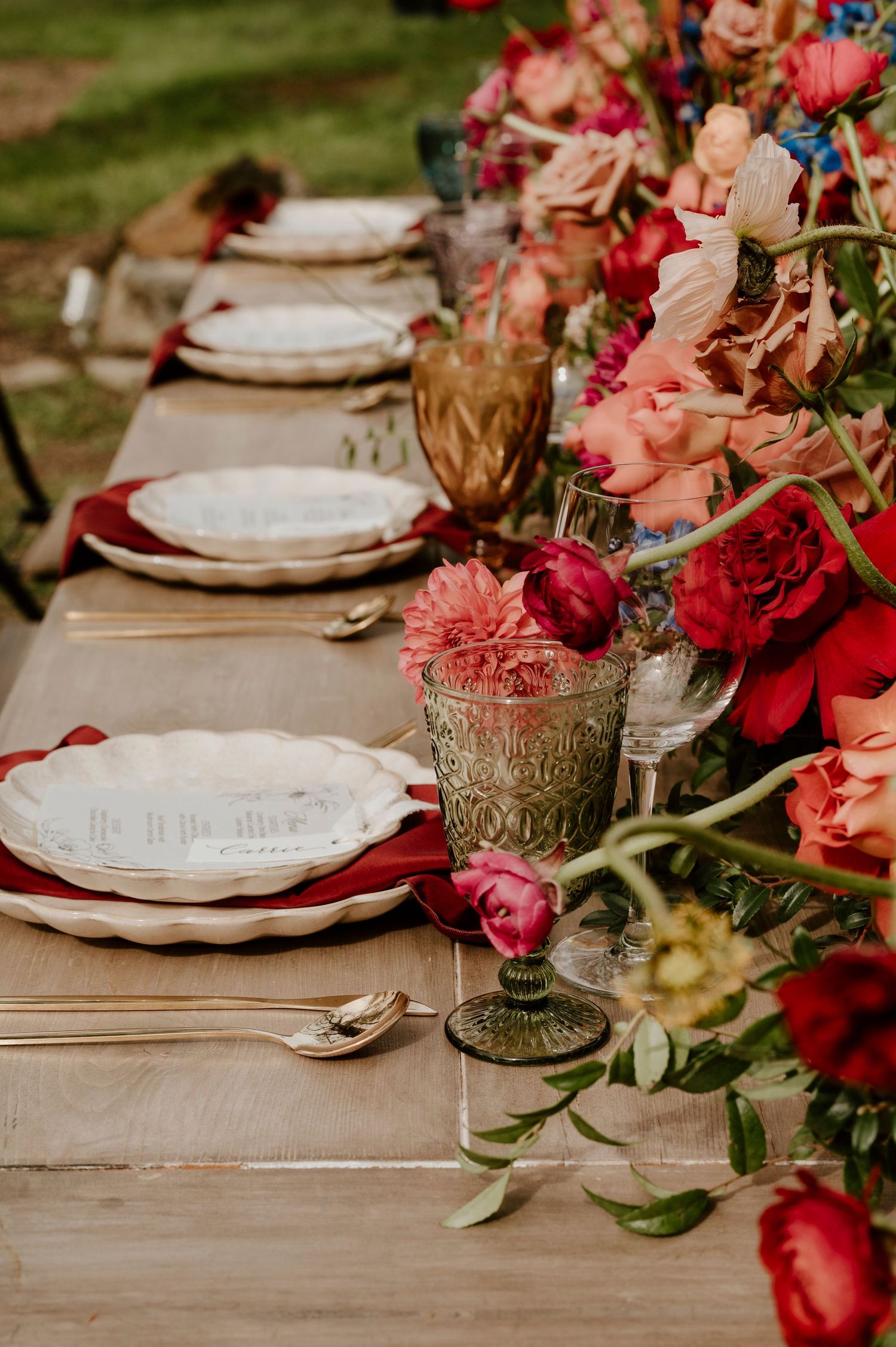Elegant table setting with white plates and coral pink floral centerpiece on wooden surface.