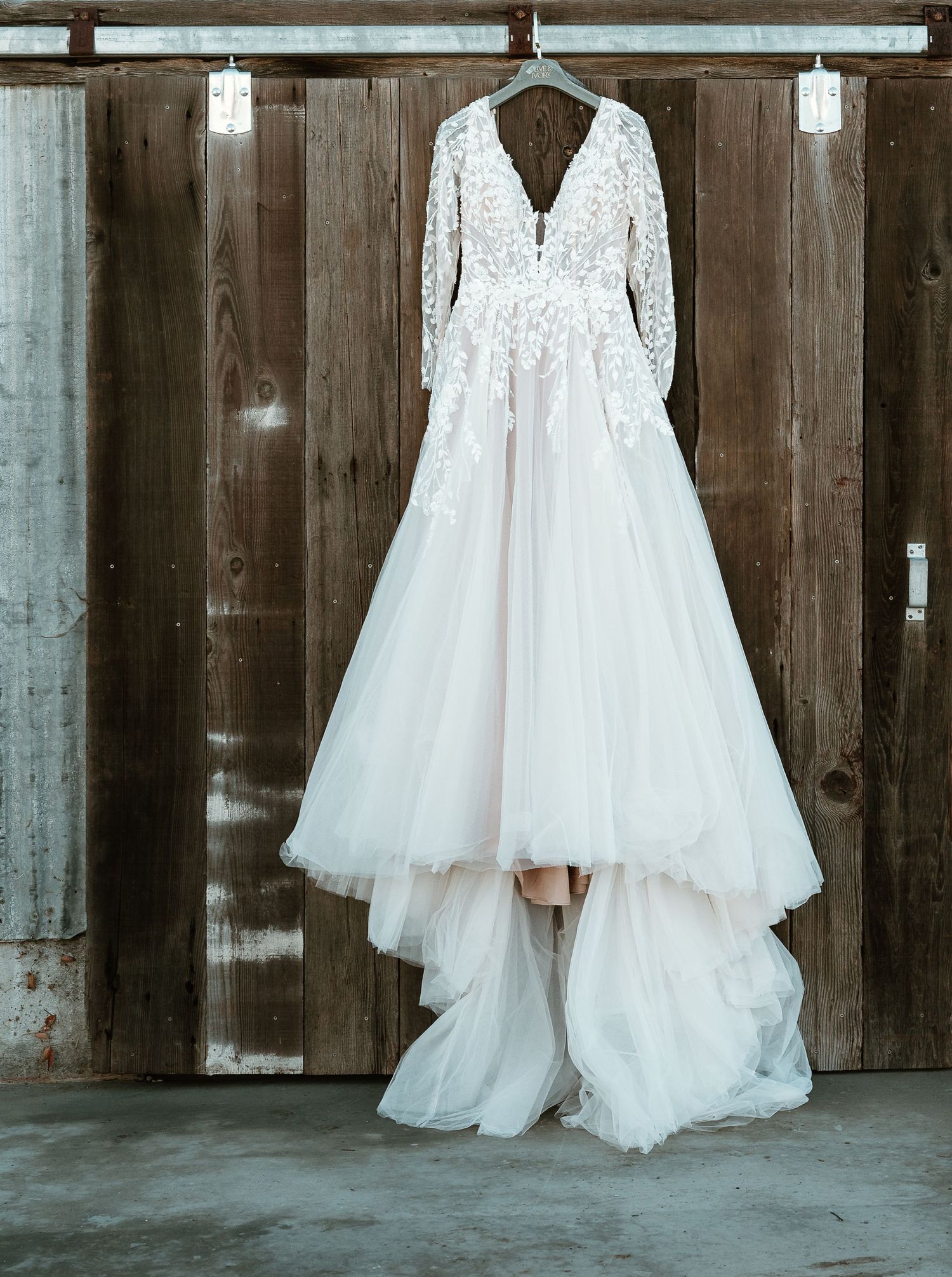 An elegant lace wedding dress with long sleeves hanging against a rustic wooden wall.