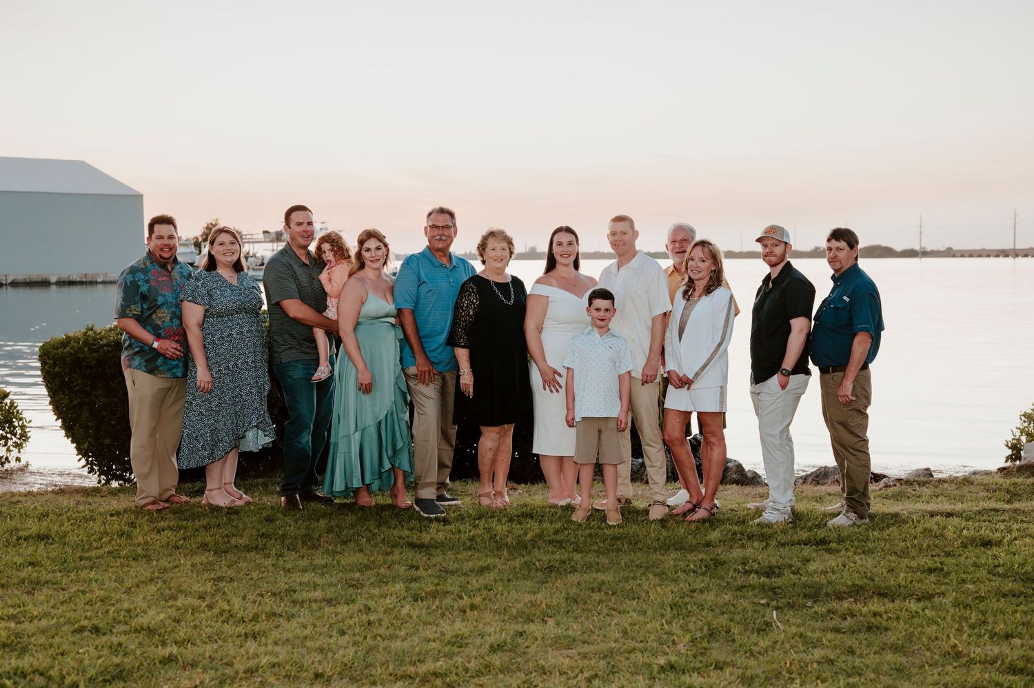 Large group photo of people gathered outdoors by the water at sunset.