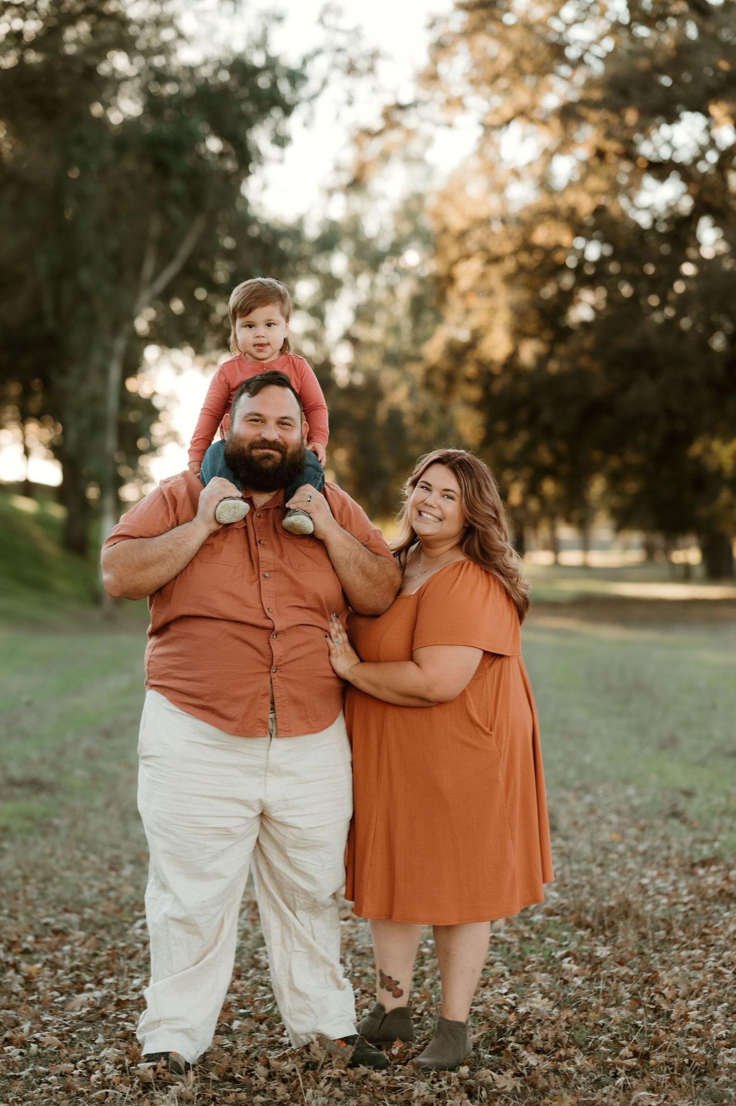 A couple in coordinated orange and white outfits share joyful moments together while sitting on fallen autumn leaves.