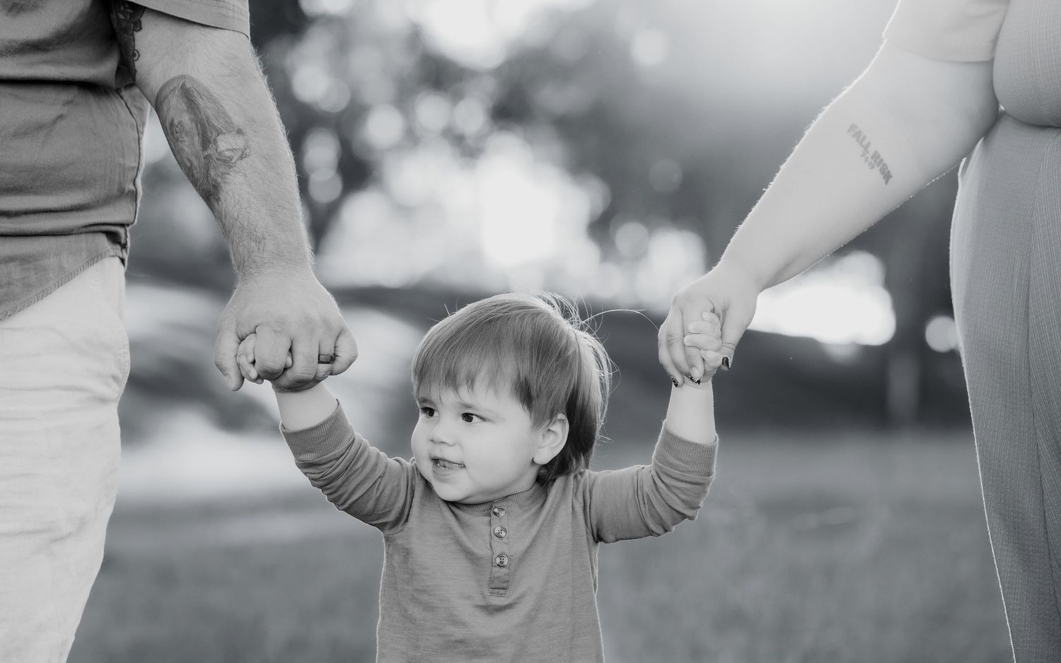 A small child holds hands with adults while walking outdoors in a black and white photograph.