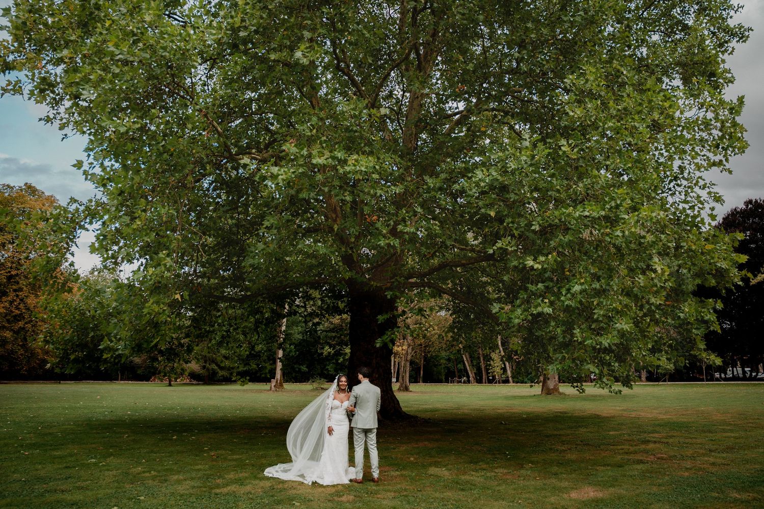 A couple in wedding attire walks together through a lush green garden setting.