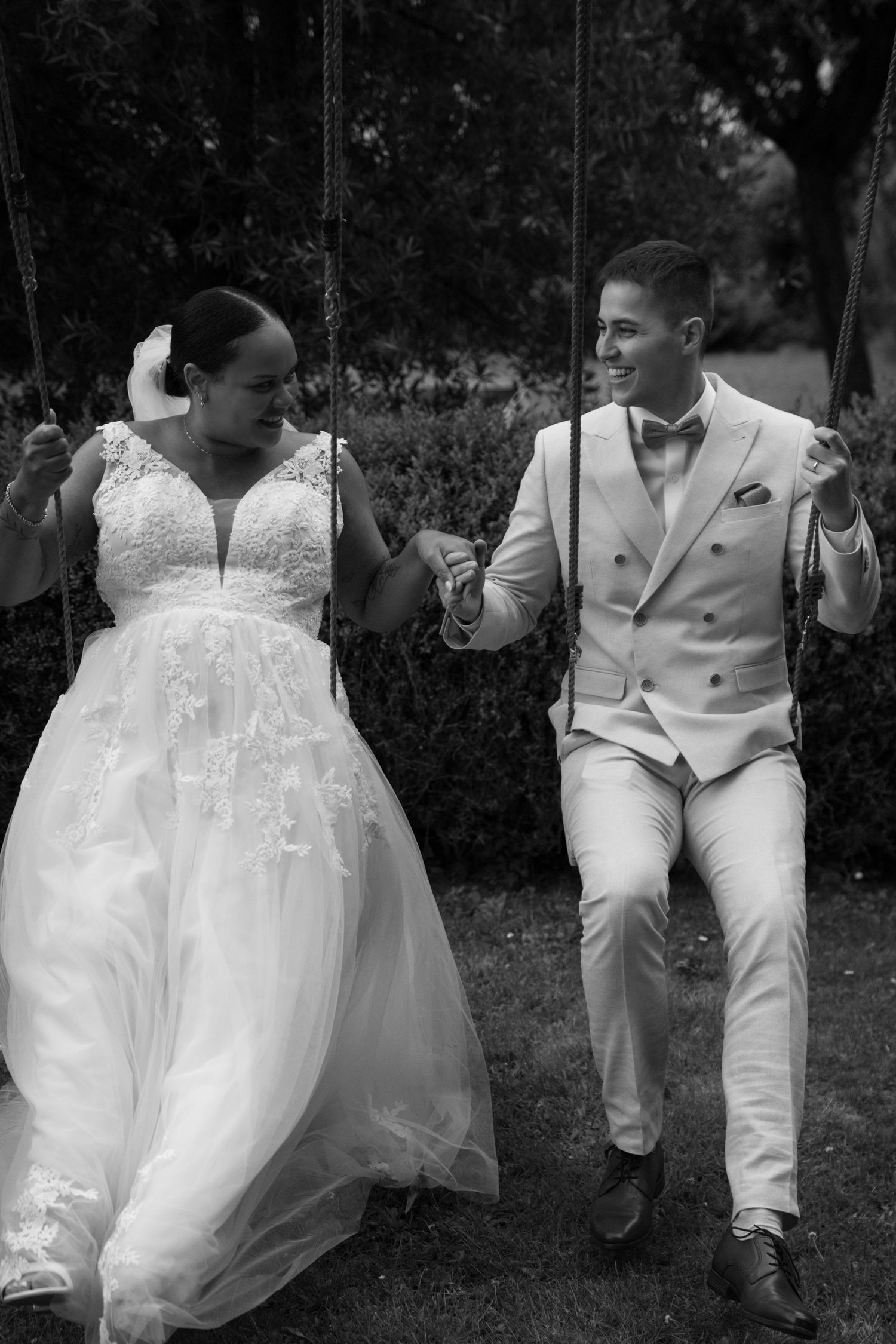 A couple in white wedding attire sits together on garden steps during an intimate moment.