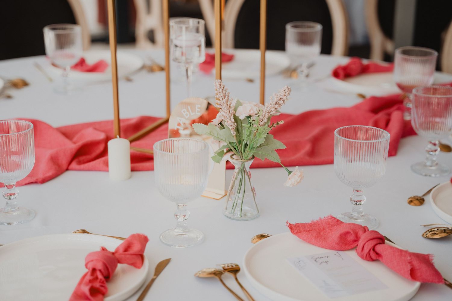 Une table de mariage dressée avec des serviettes corail, des touches dorées et de délicats centres de table floraux.