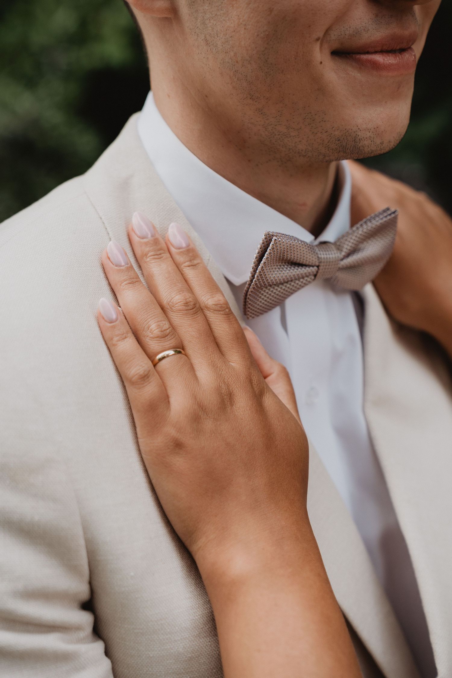 Close-up of hands touching a bowtie, with a gold wedding band visible.