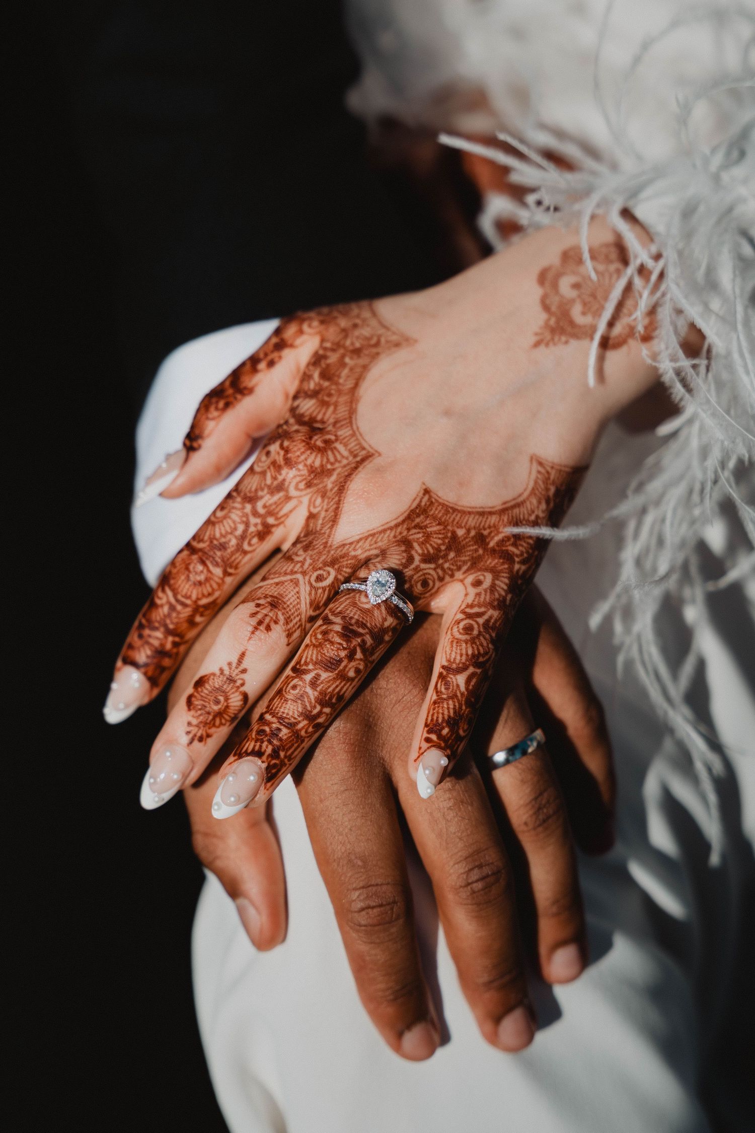 Des motifs détaillés au henné ornent les mains, avec des détails de bague de fiançailles et de dentelle blanche.