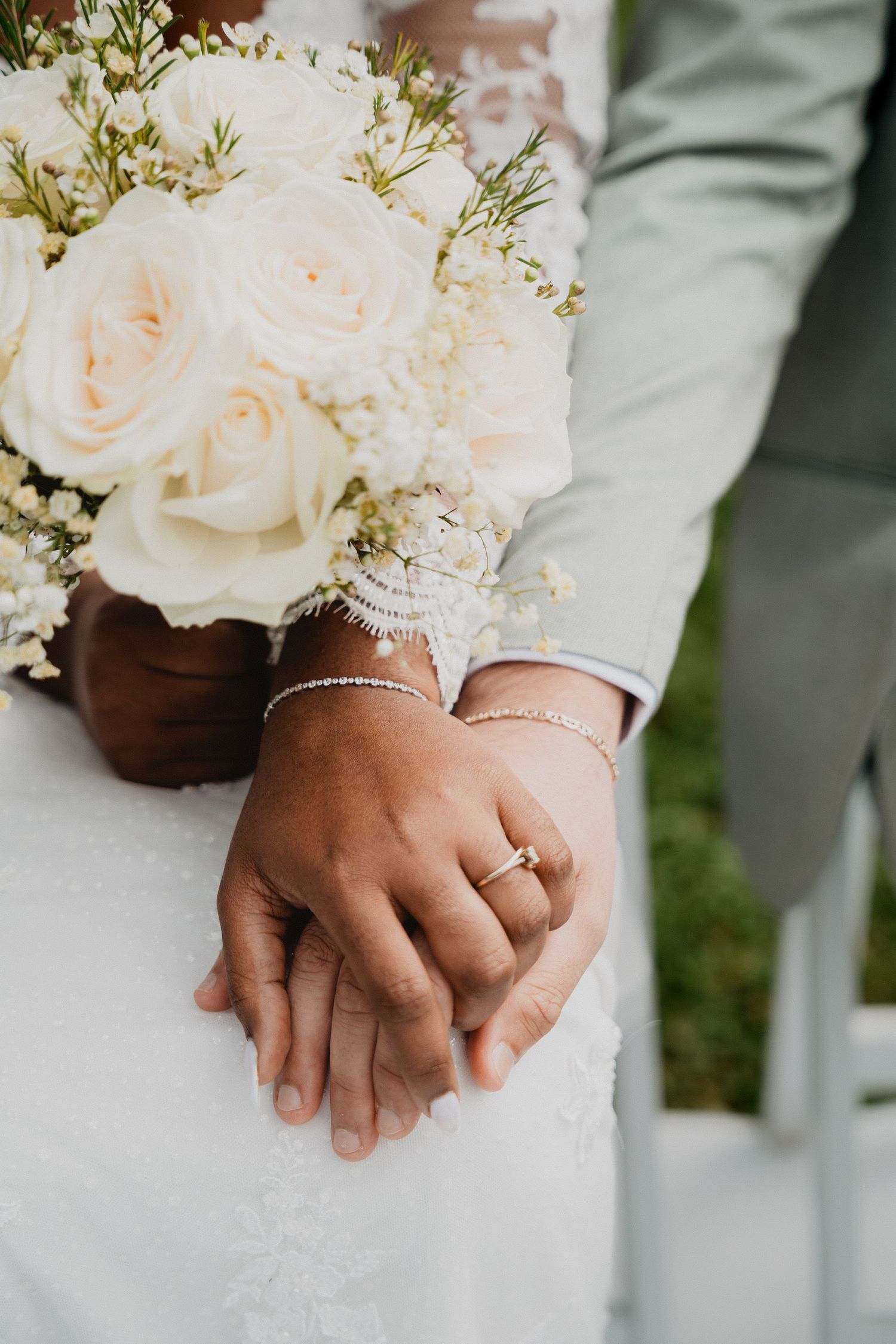 Gros plan sur des mains portant des alliances et tenant des bouquets de roses blanches.