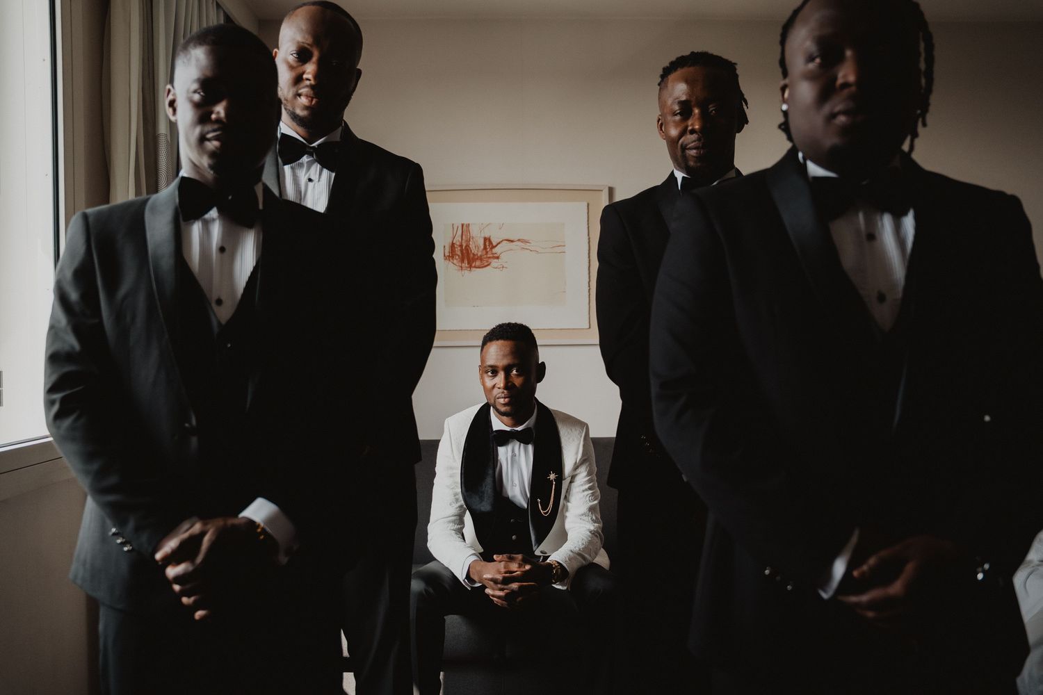Les membres du cortège nuptial, vêtus de tenues formelles noires et blanches, posent ensemble pour un portrait d'intérieur à l'atmosphère my