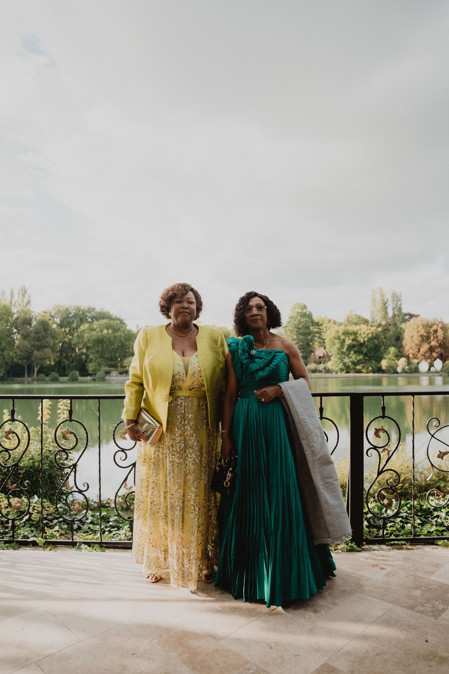 Les invités du mariage, vêtus de robes élégantes, posent sur un balcon à la balustrade ornée.