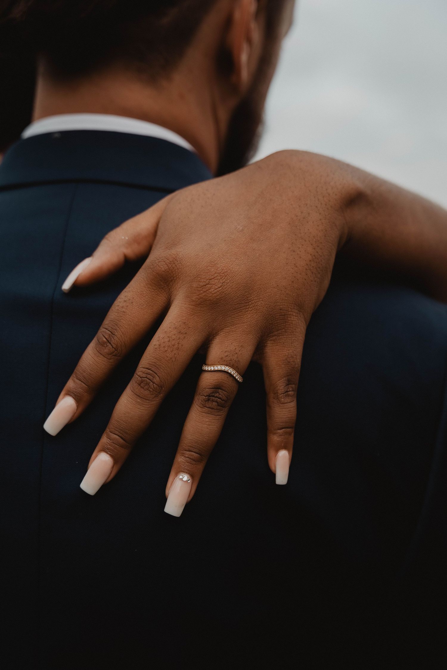 Close-up of manicured hands with white acrylic nails wearing a wedding ring.