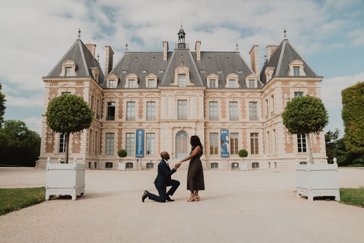 Un grand château français à l'architecture élégante et aux jardins soignés, au moment d'une demande en mariage.