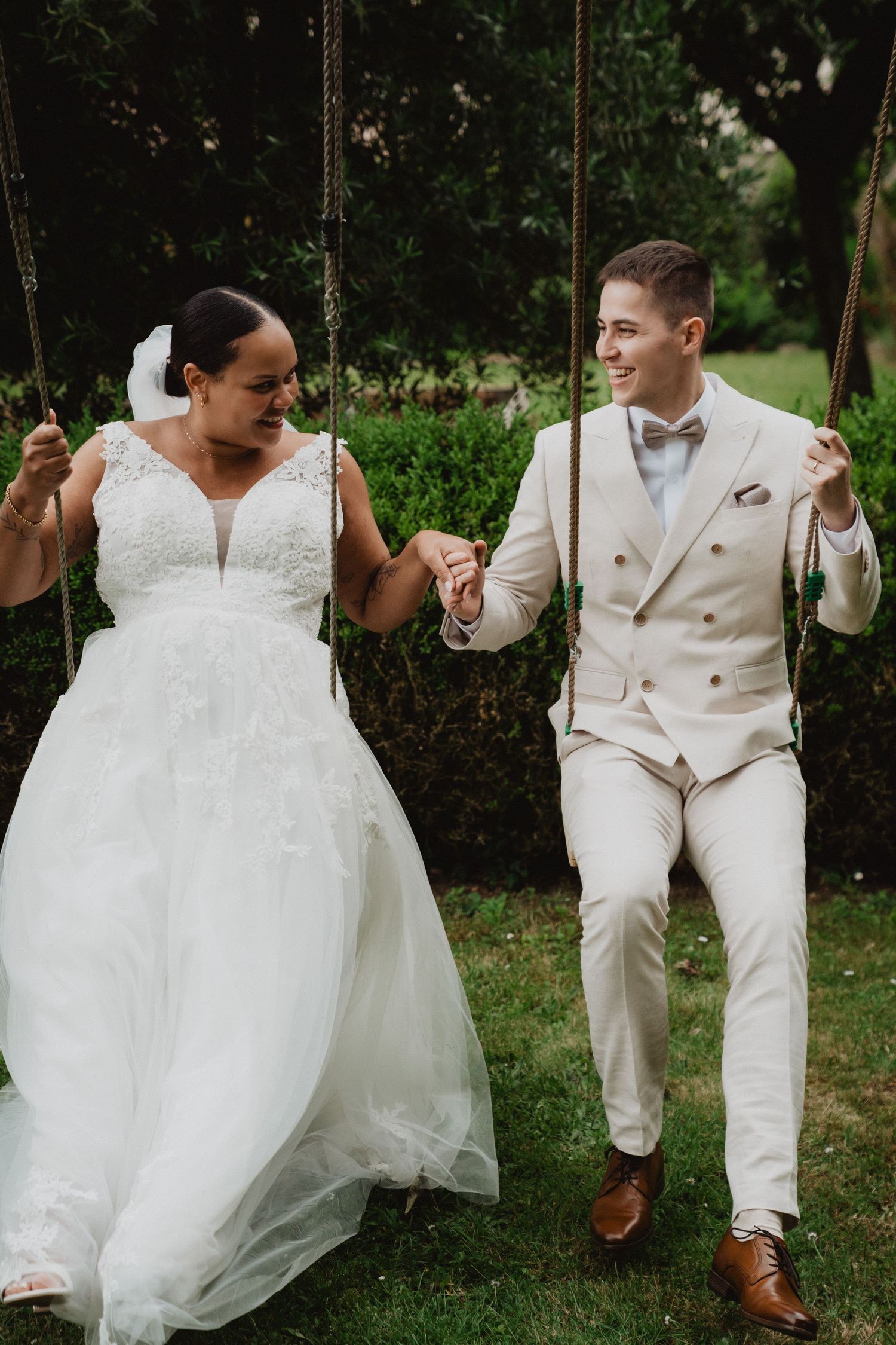 A joyful couple in wedding attire sharing a playful moment on a garden swing.