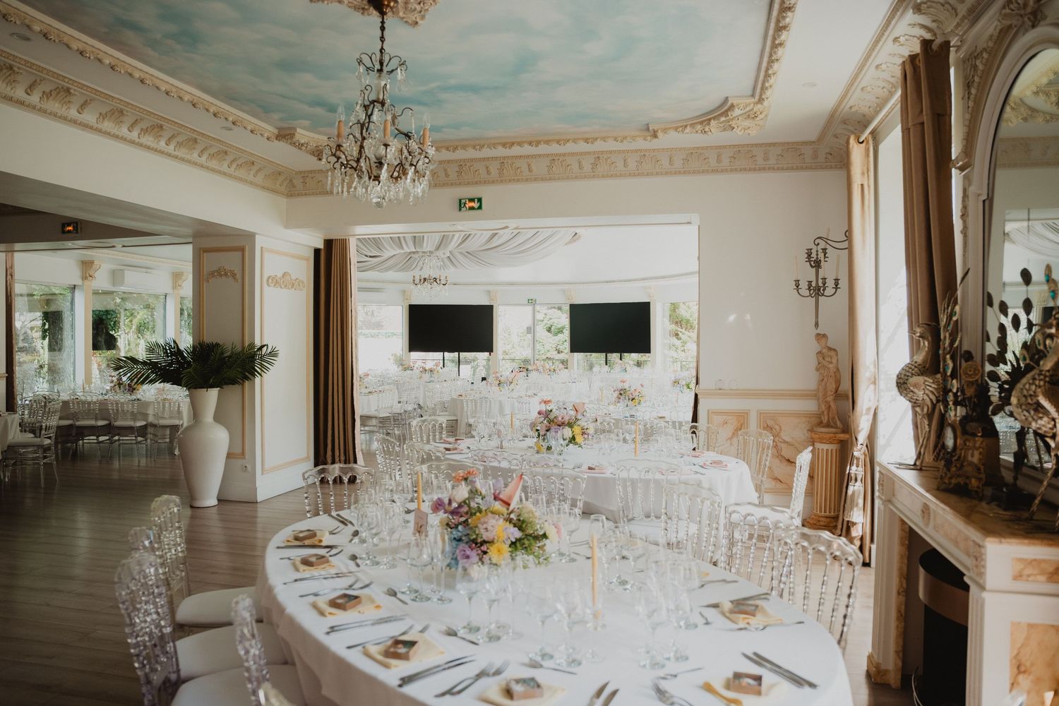 Salle de réception de mariage élégante avec plafond orné, lustres et tables dressées.