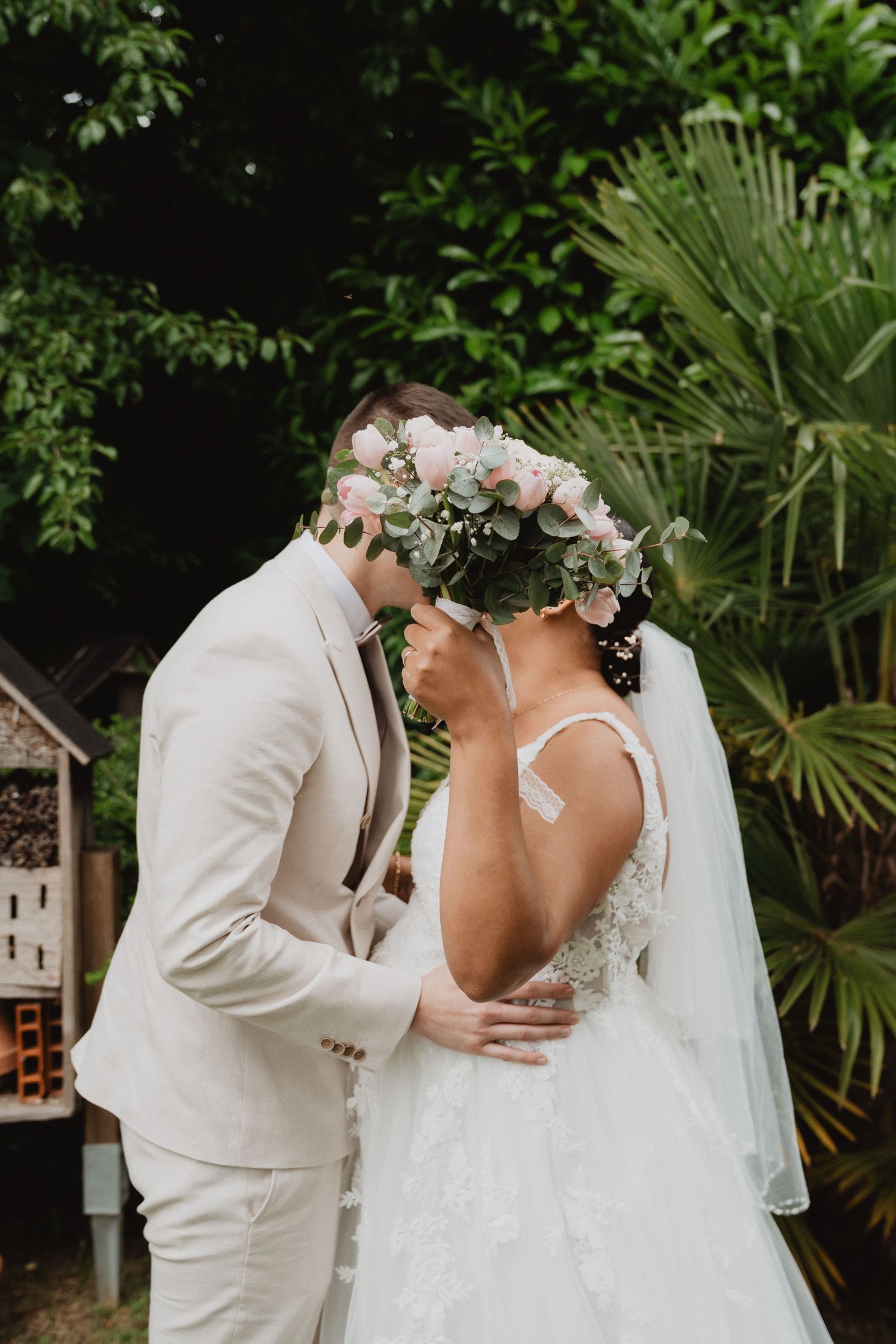 A romantic wedding moment captured in a lush garden setting with tropical plants.