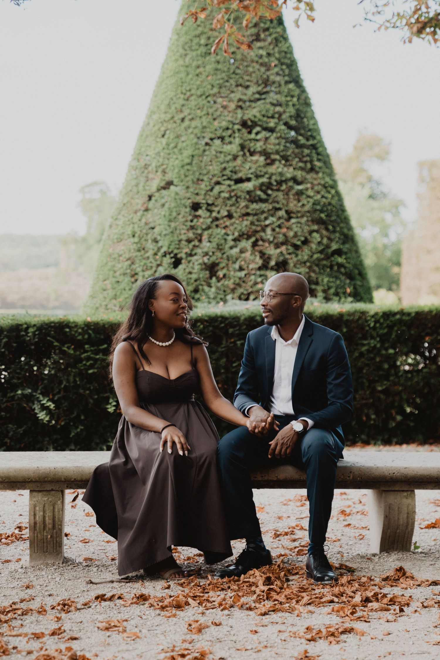 Une séance photo romantique d'automne avec un couple assis sur des bancs de pierre, entourés de feuilles mortes.