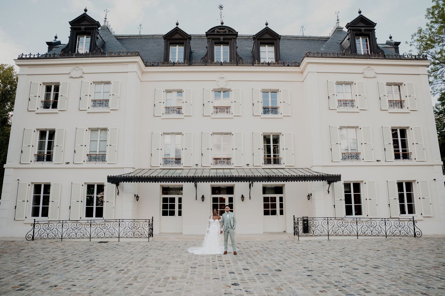 A grand white mansion with dormer windows and classic French architecture stands against a bright sky.