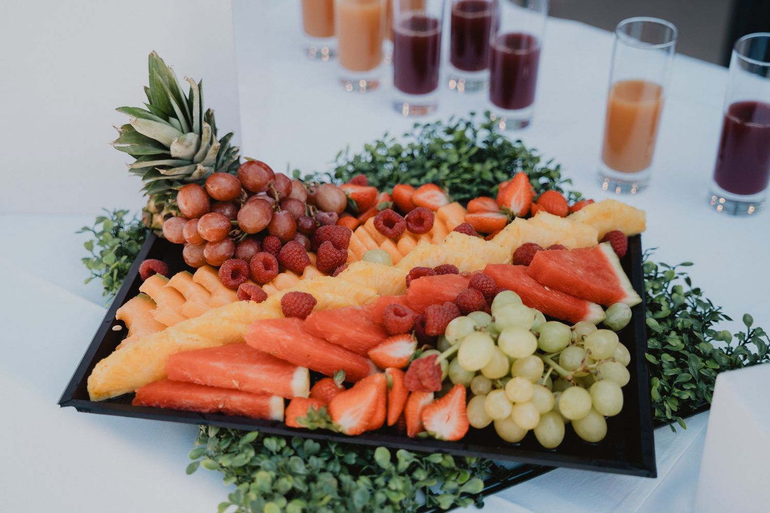 Une table de mariage dressée avec des serviettes corail, des touches dorées et de délicats centres de table floraux. Un plateau de fruits et