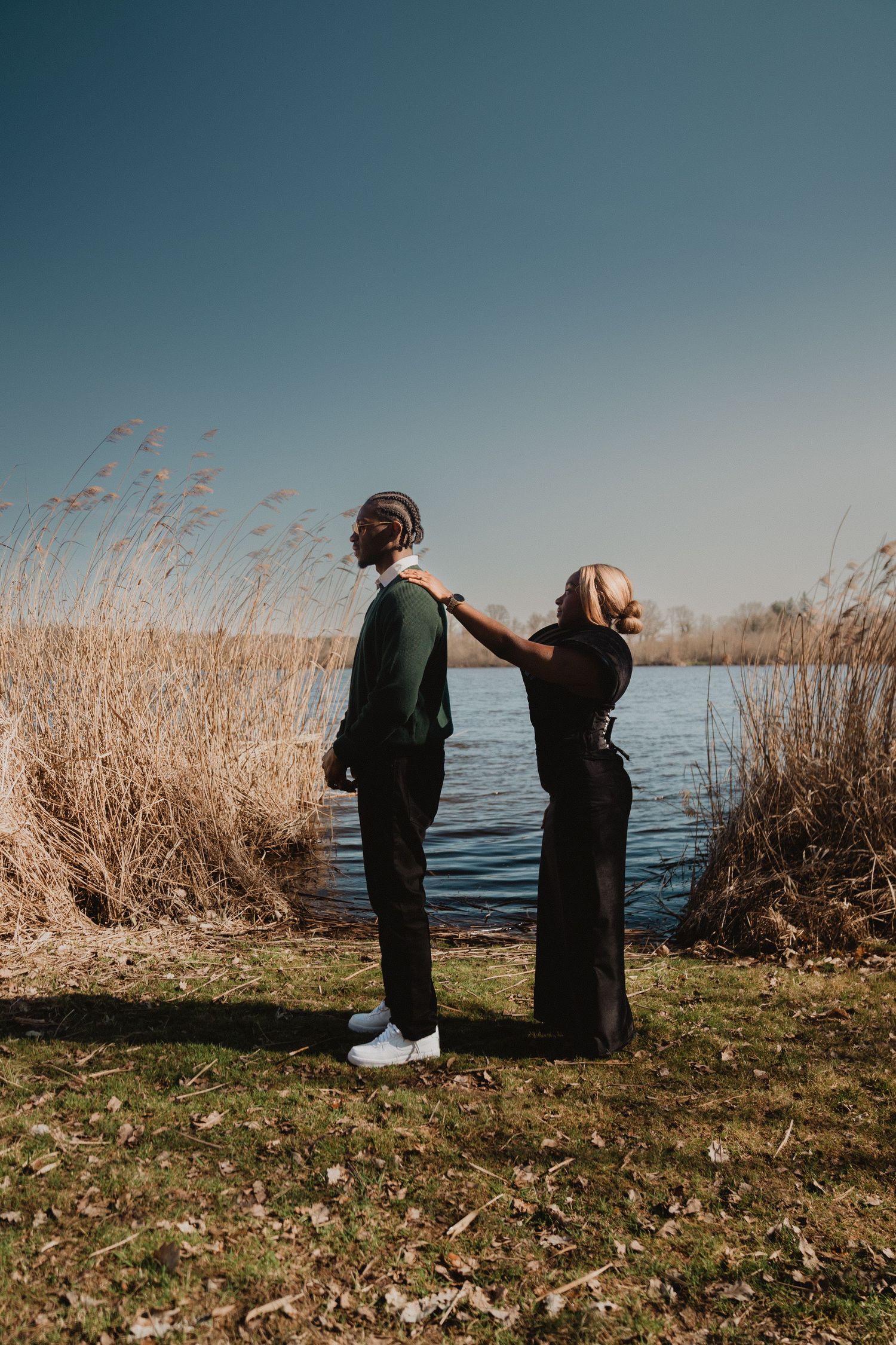 Un couple se tient au bord du lac, parmi les hauts roseaux, à l'heure dorée.