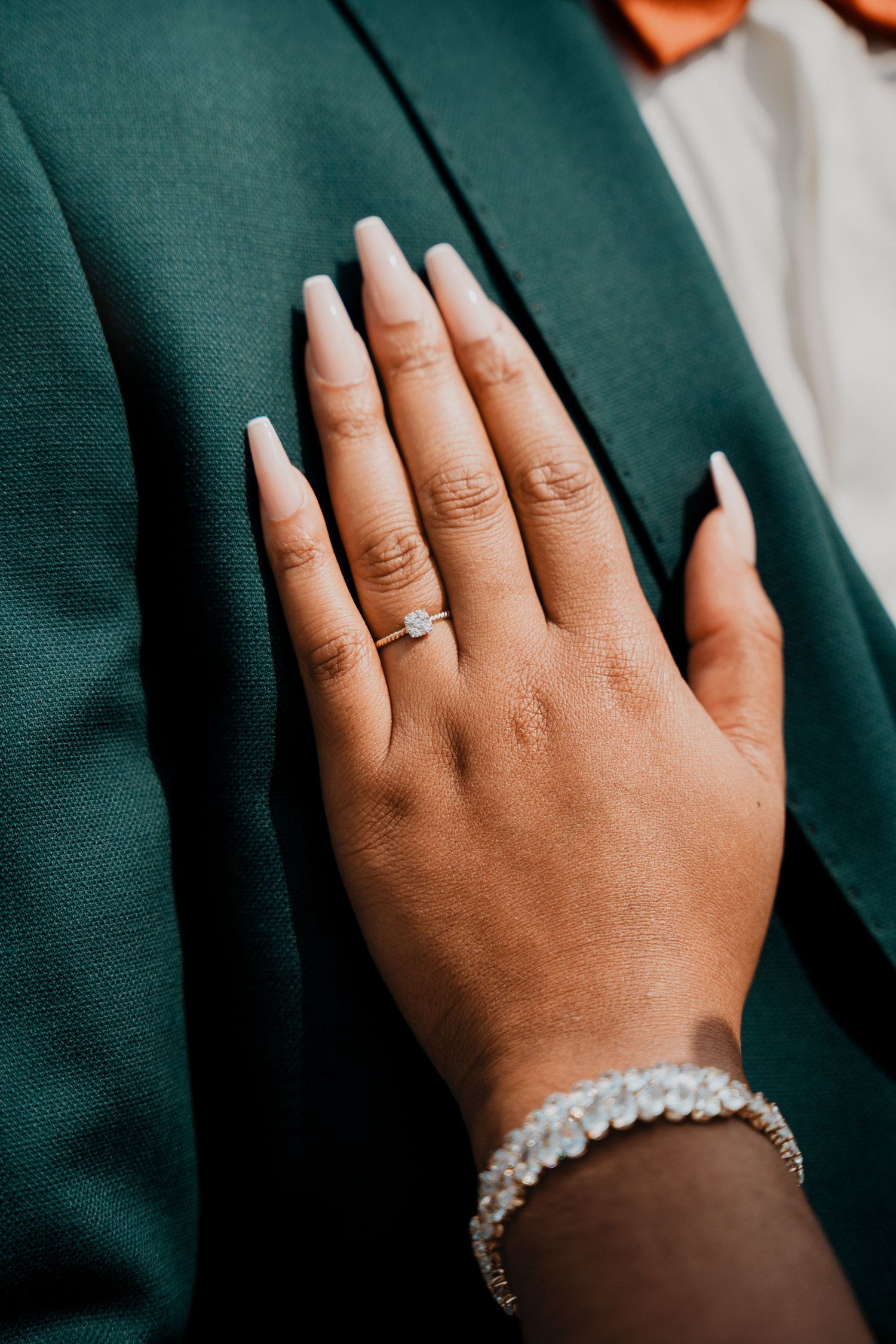 Gros plan sur des mains portant une bague de fiançailles et un délicat bracelet en cristal sur un tissu vert foncé.