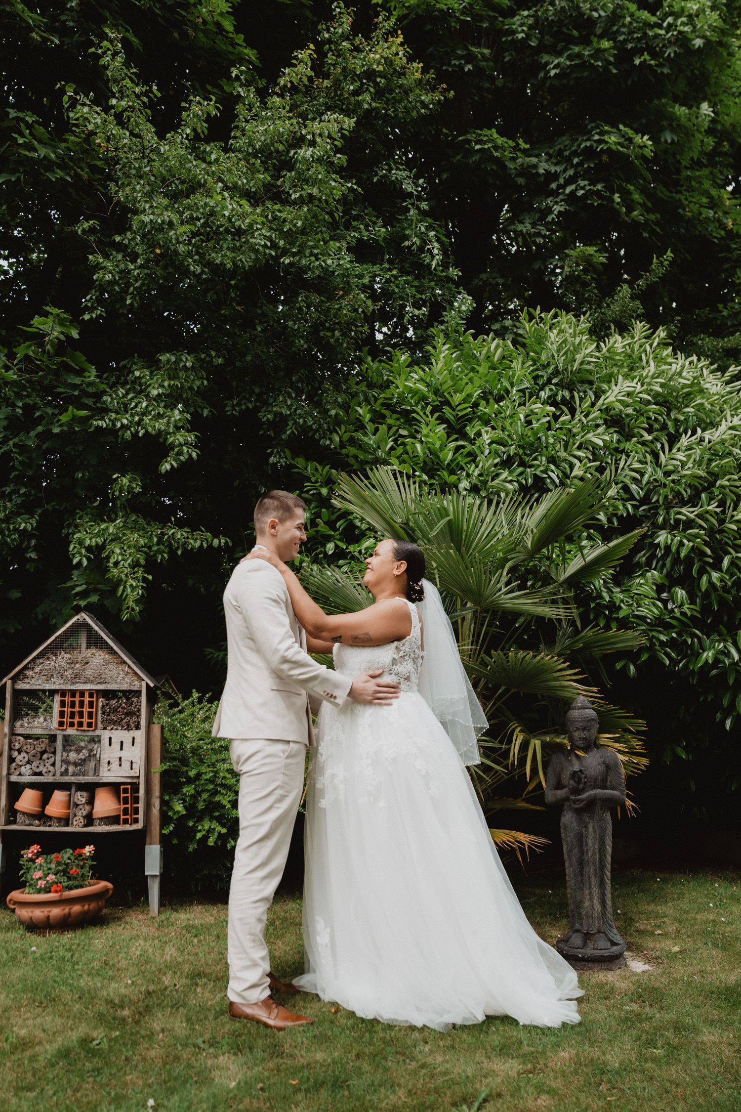 A couple shares a playful moment in a garden setting with an insect hotel visible in background.