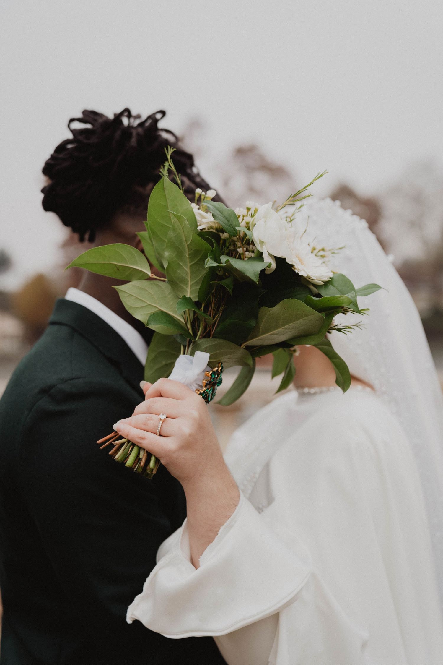 Wedding couple holding white floral bouquets against a light background.