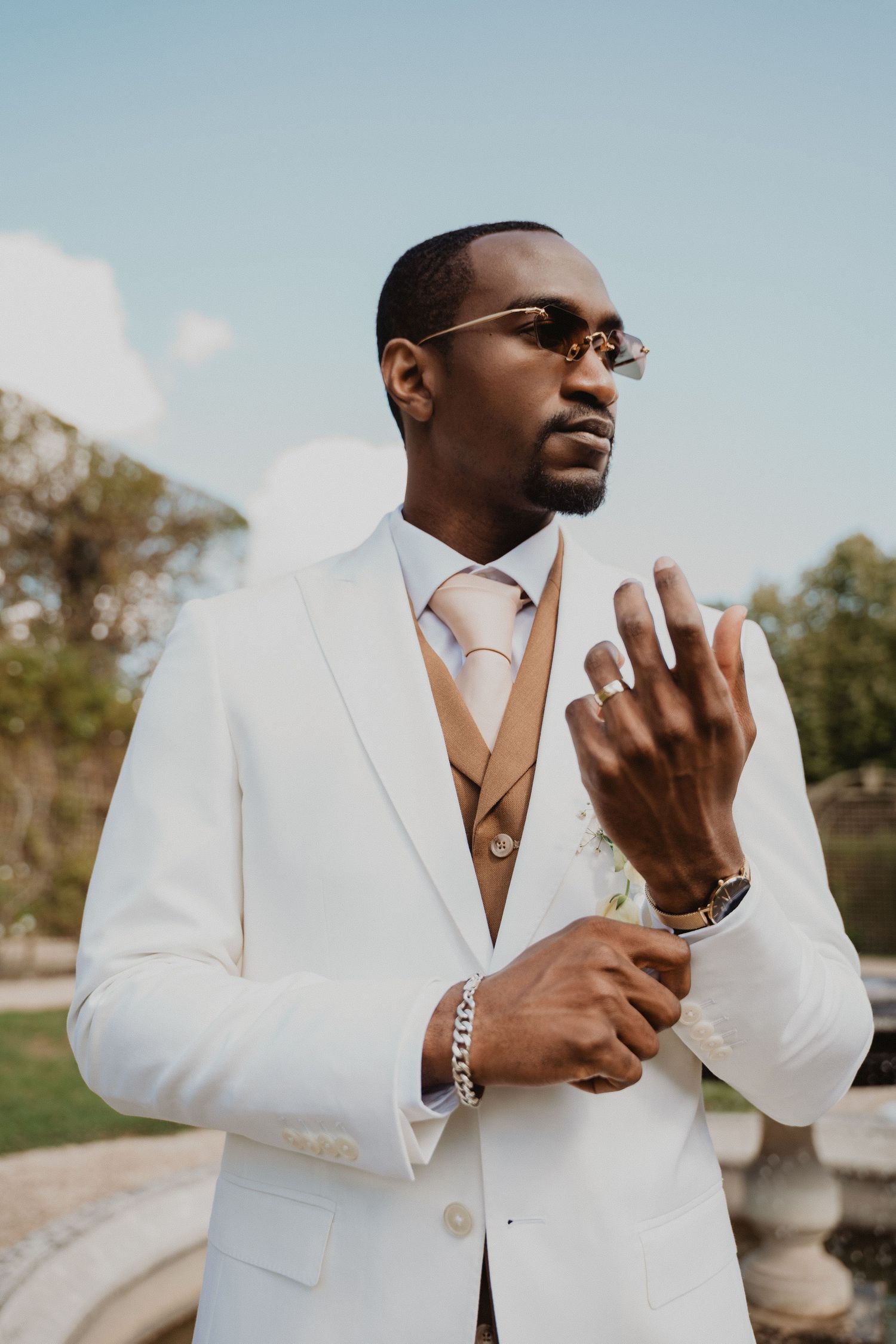 Stylish groom in white suit and sunglasses making expressive gestures.