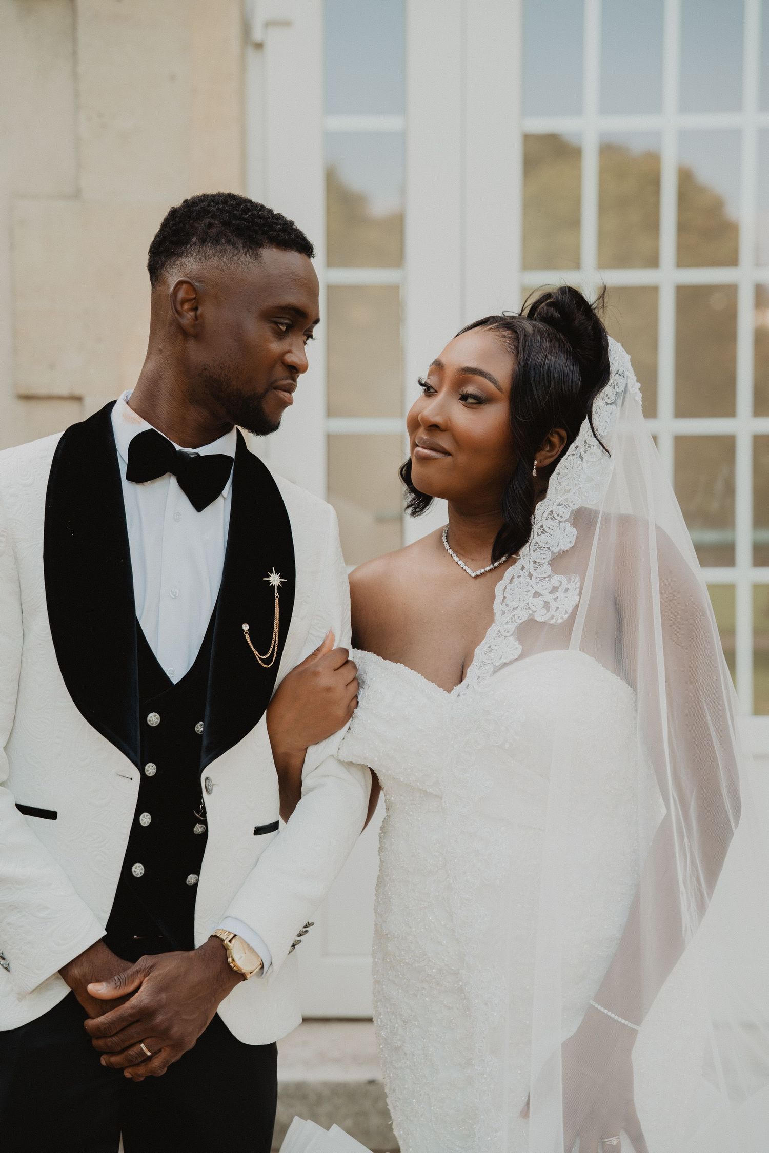 Élégants portraits de mariage devant un immeuble blanc aux grandes fenêtres.