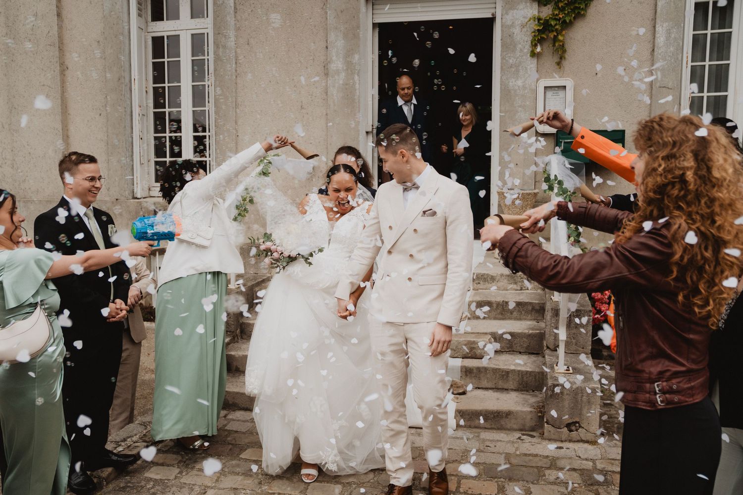 Les invités du mariage aspergent les jeunes mariés de confettis à leur sortie du bâtiment, en pleine célébration.