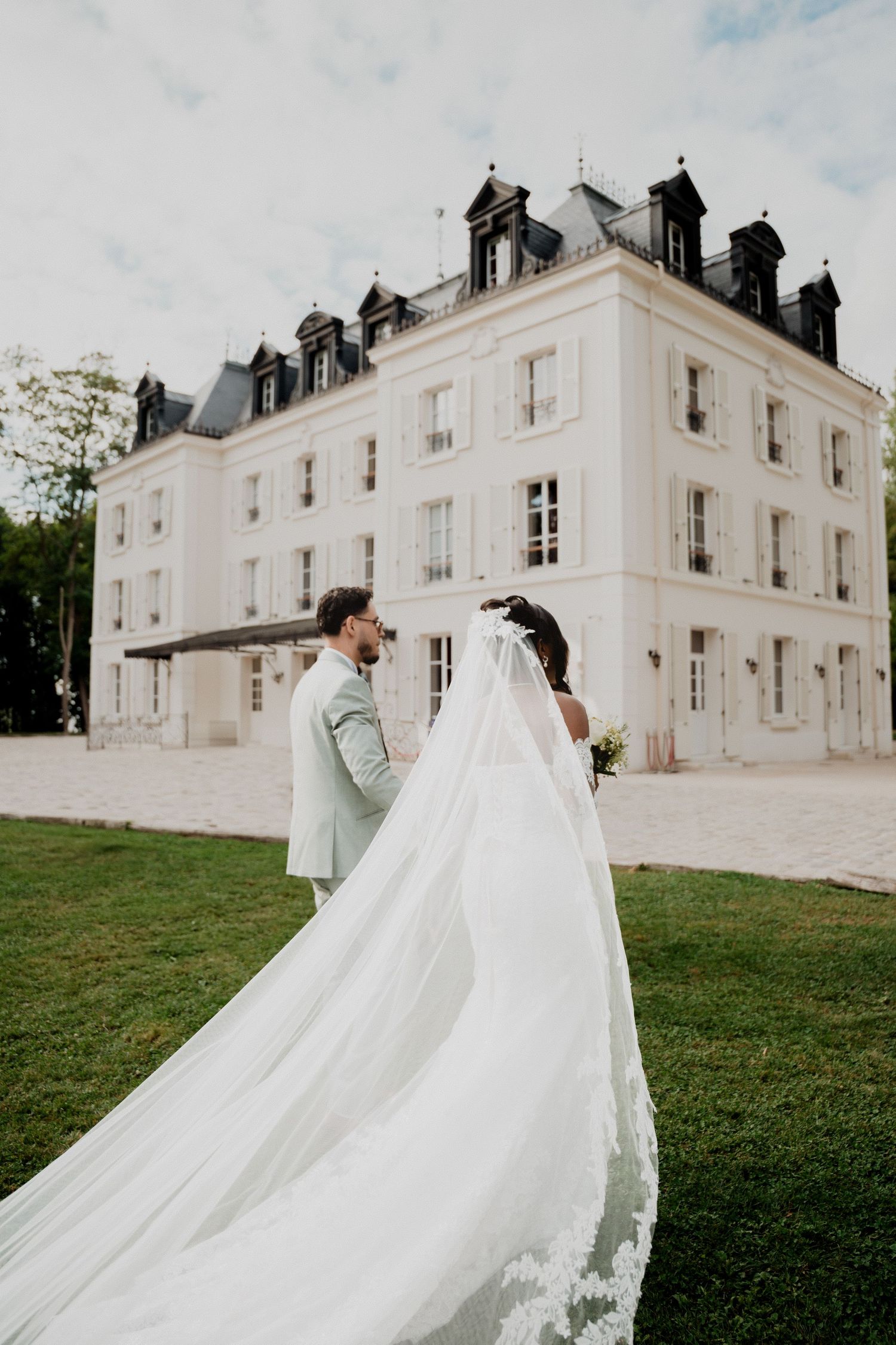 Flowing white wedding gowns create dramatic silhouette against classic French chateau.