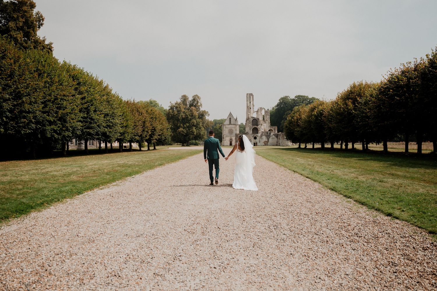 Un long chemin bordé d'arbres mène à un couple au loin, en pleine séance photo romantique.