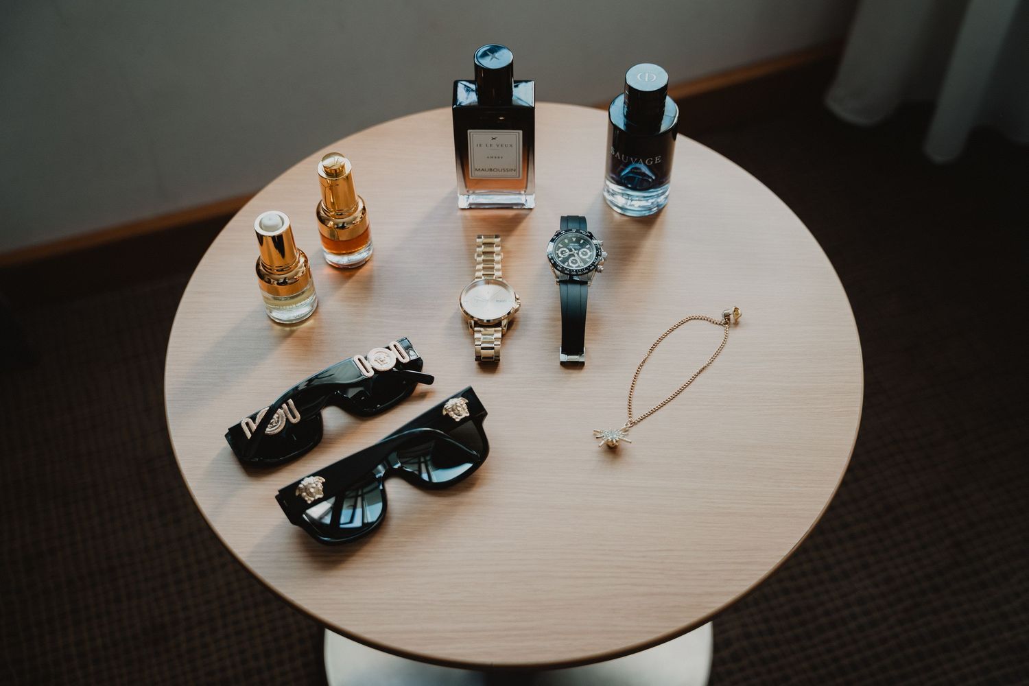 Accessoires de mariage disposés sur une table ronde, notamment des montres, des lunettes de soleil et des flacons de parfum.