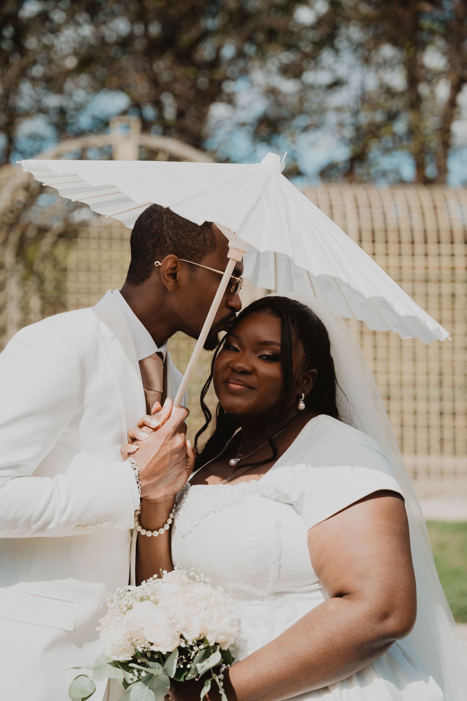 Intimate wedding moment captured under a white parasol in an outdoor setting.