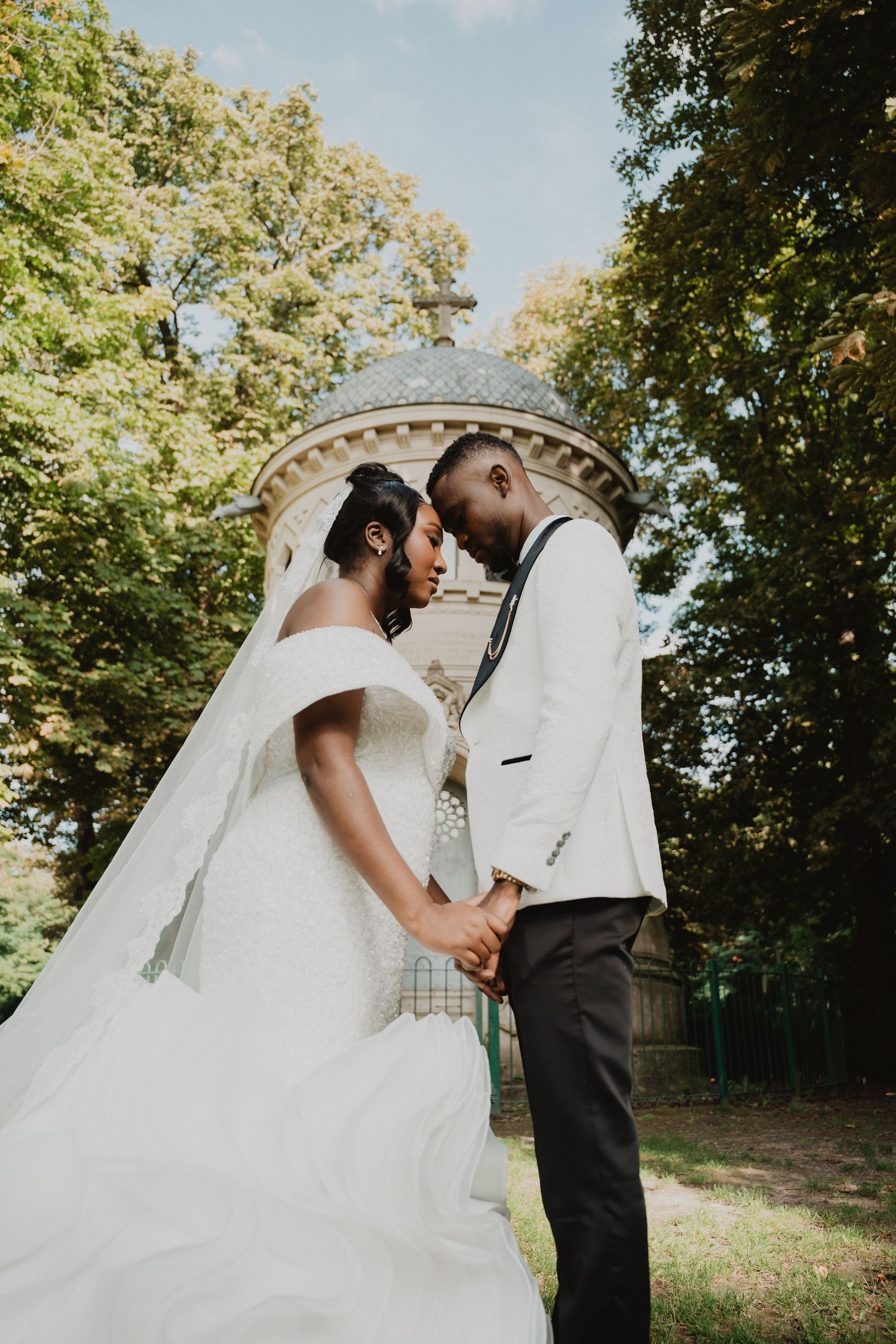 A romantic moment between newlyweds in front of a Victorian-style tower surrounded by trees.