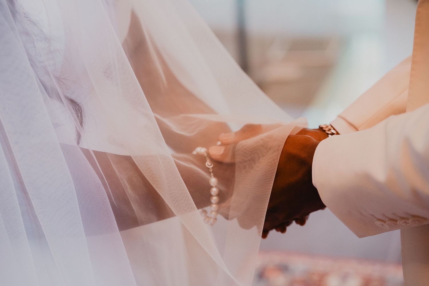 Close-up of hands joining during a wedding ceremony with delicate white veil details.