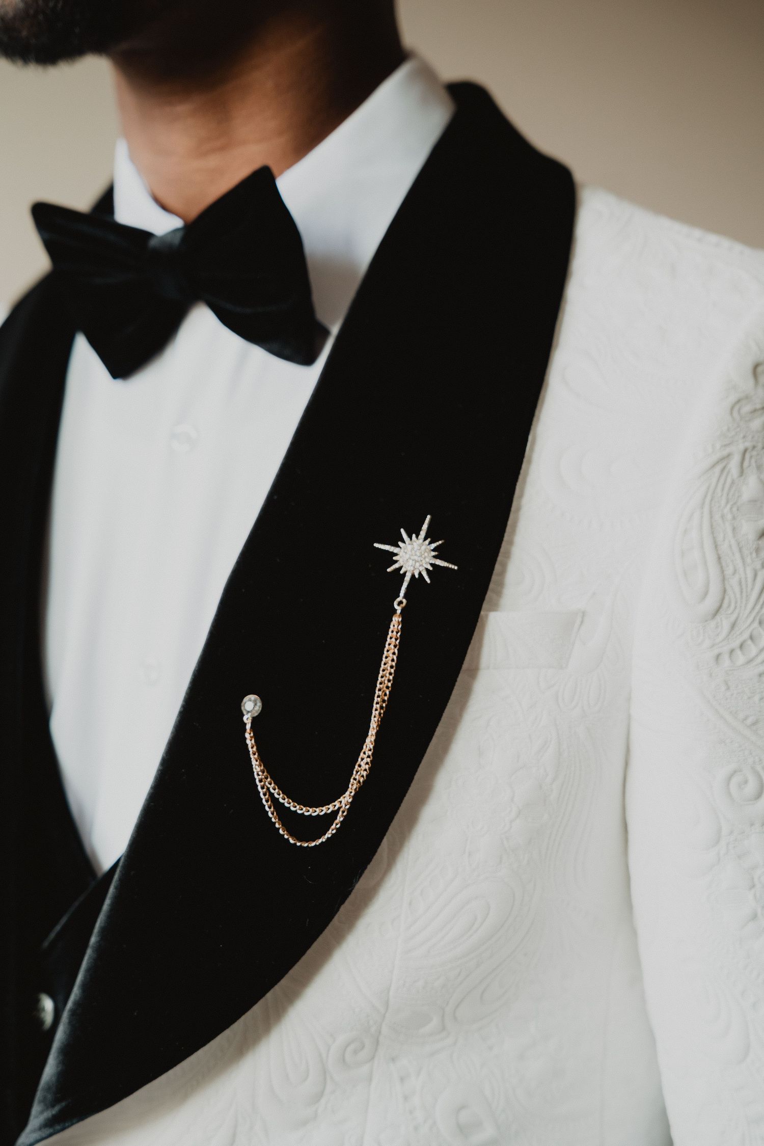 Gros plan sur les détails d'une veste de smoking blanche à revers noirs et accessoire de chaîne décorative.